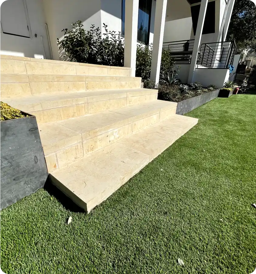 Stone staircase leading down to an artificial turf lawn in Austin, Texas.