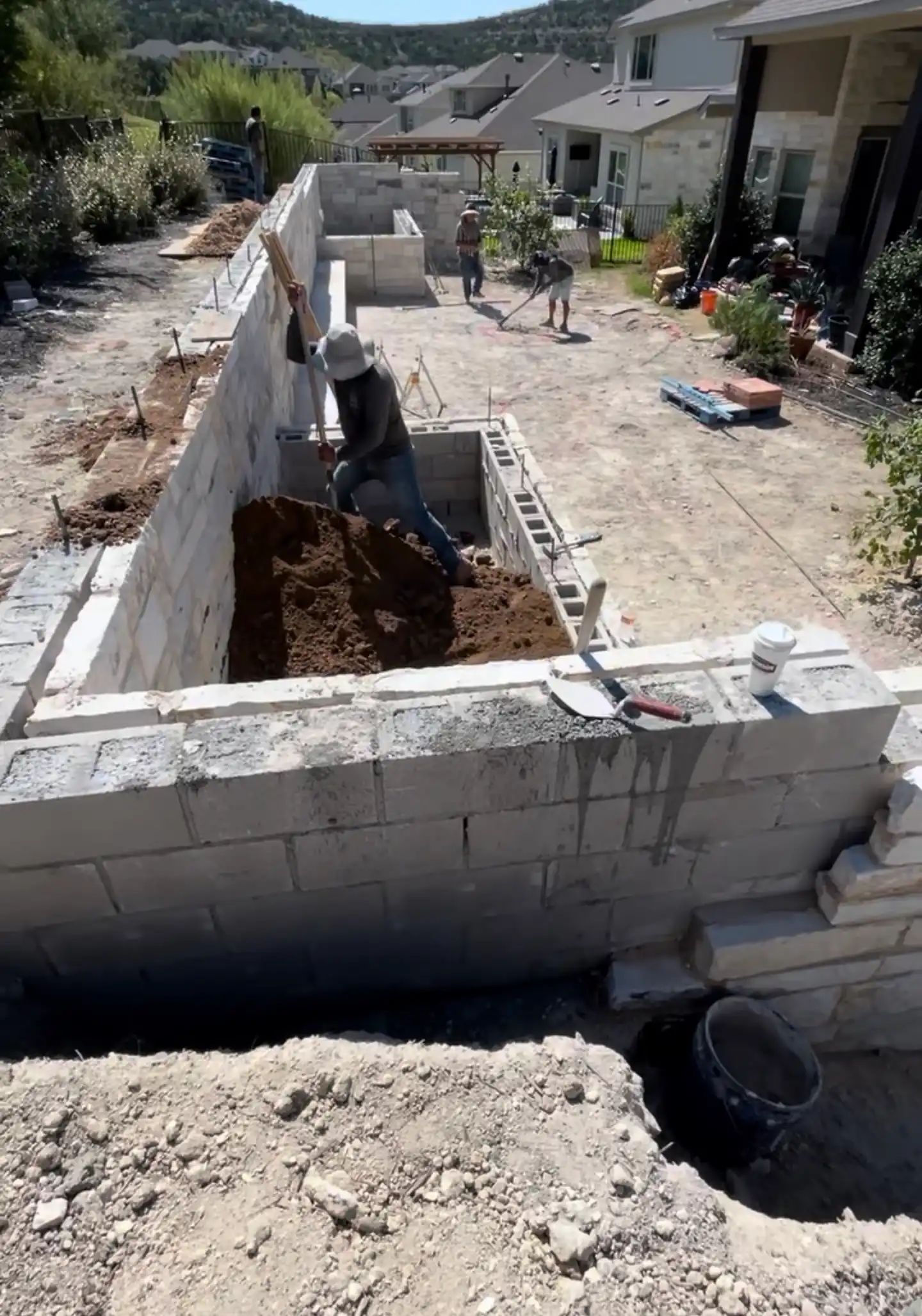 Concrete block retaining wall under construction with a drainage trench in an Austin backyard