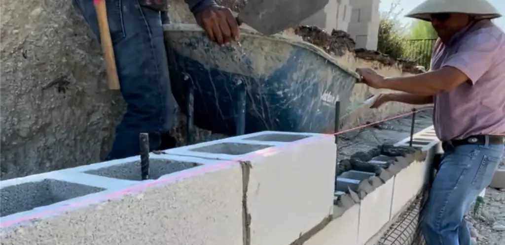 Masons laying and mortaring a concrete block retaining wall during construction in Central Texas