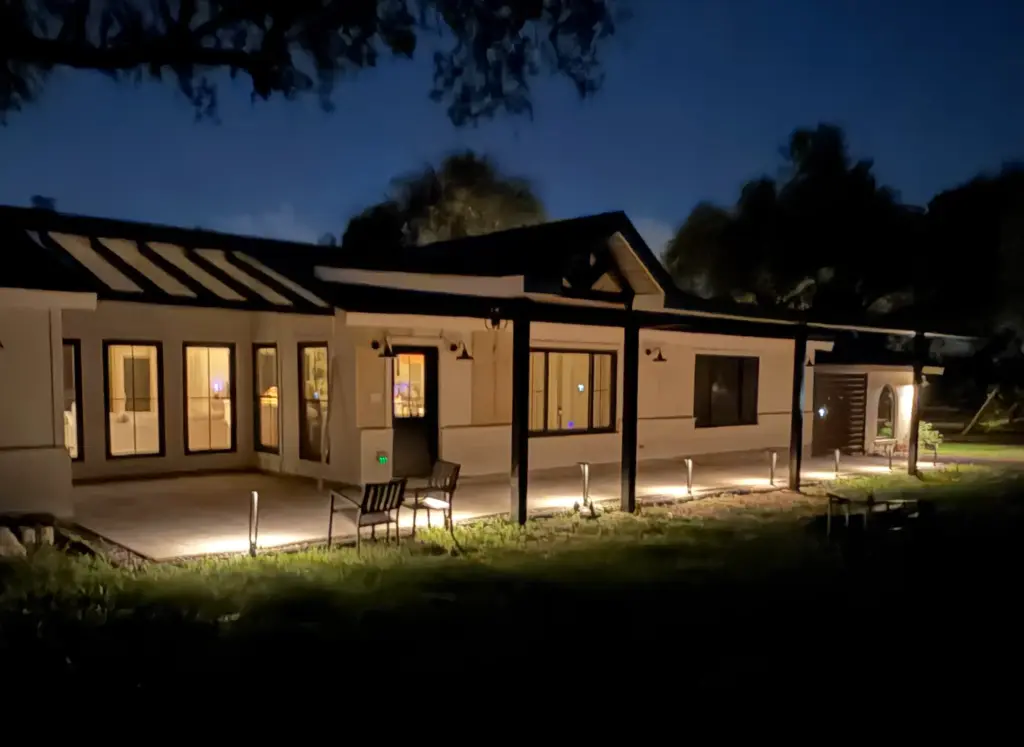 Hardscape 10 Outdoor Living Space Ideas Worth Stealing for Your Austin Backyard 1 Covered stone patio with landscape lighting along a white stucco home at dusk