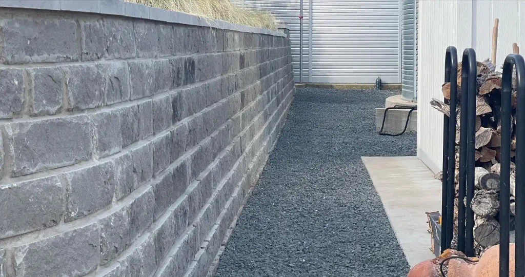Gray stone block retaining wall beside a gravel side yard path